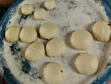 Close-up image of several raw dough balls resting on a floured surface, with a few flies landing on the dough.の写真素材