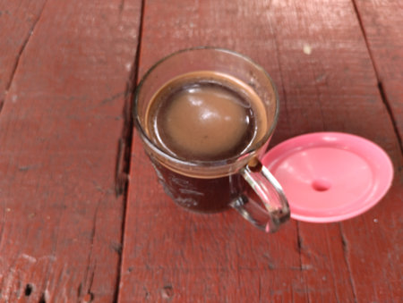 A top-down view of a hot black coffee served in a clear glass cup placed on a rustic red wooden table.の写真素材