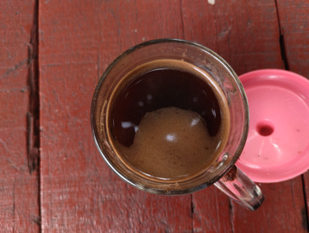 A top-down view of a hot black coffee served in a clear glass cup placed on a rustic red wooden table.の写真素材