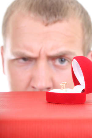 young man looking at wedding ring in red box. Focus on ringの写真素材