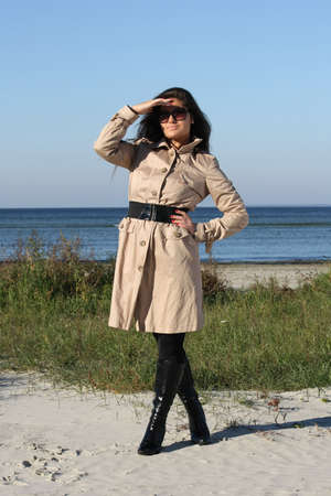 beautiful woman in beige autumn coat and  sunglasses posing by the seaの写真素材
