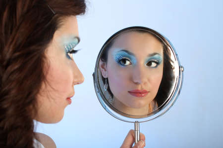 beautiful woman with make-up looking at mirror over blue backgroundの写真素材