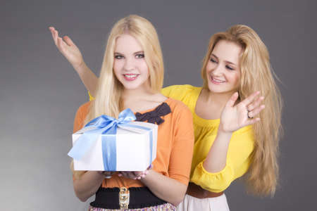 attractive woman giving a present to her surprised friend over greyの写真素材