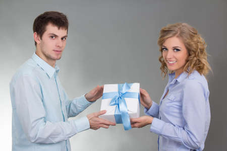 young man giving a gift to his beautiful girlfriend over greyの写真素材