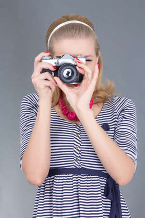pinup woman in retro clothes posing with photo camera over greyの写真素材