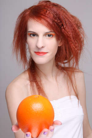portrait of young curly redhaired woman with orangeの写真素材