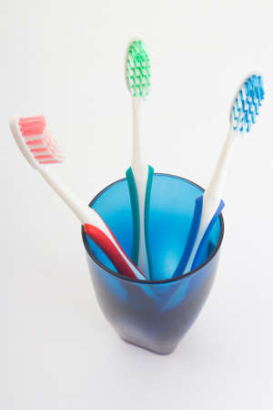 colorful toothbrushes in blue glass over whiteの写真素材