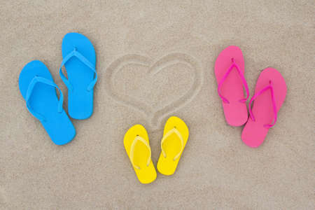 blue, red, yellow flip flops and heart on the beachの写真素材