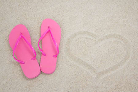 pink flip flops and heart on white beach sandの写真素材