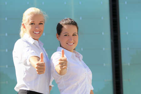 portrait of two young attractive business women with thumb upの写真素材