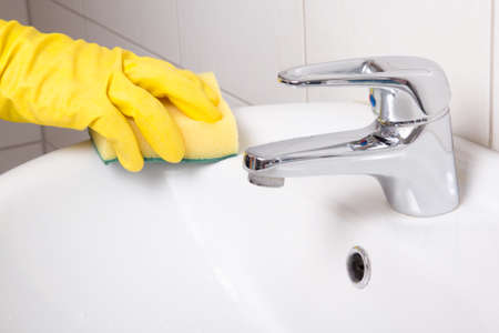 Hand in yellow glove with sponge cleaning white sinkの写真素材