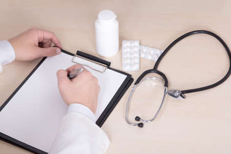close up of male doctor's hands, stethoscope and pills on the tableの写真素材