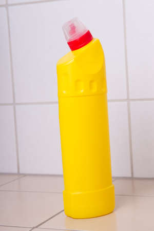 yellow plastic bottle of cleaning product on tiled floor in bathroom