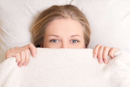 happy young beautiful woman lying in bed under blanket