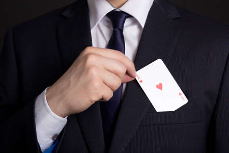 mans hand hiding playing card in business suit pocketの写真素材