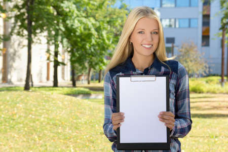 young beautiful woman showing clipboard with copyspace in autumn parkの写真素材