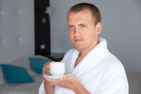 happy young man in bathrobe drinking coffee in hotel roomの写真素材