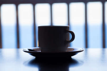 dark picture of cup of coffee on wooden table over sea viewの写真素材