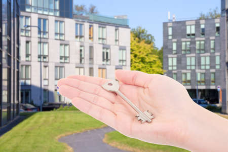 real estate concept - female hand with metal key over modern buildingの写真素材
