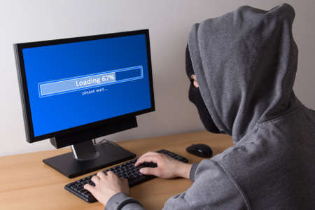 male thief in mask stealing data from computer