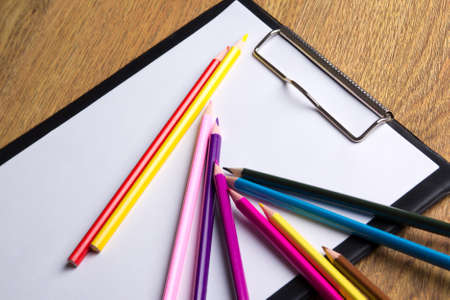 close up of many colored drawing pencils and clipboard with blank paper on wooden table backgroundの写真素材