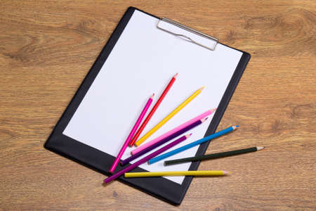 colorful drawing pencils and clipboard with blank paper on wooden table backgroundの写真素材