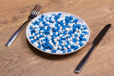 diet concept - blue pills in plate with knife and fork on wooden tableの写真素材