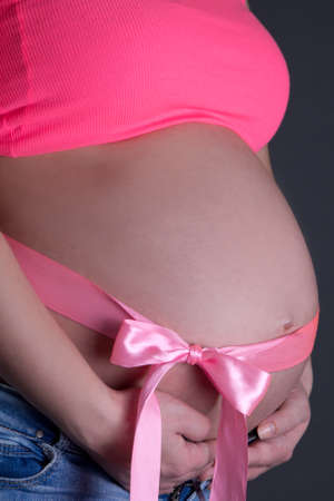 pregnant woman's belly with pink ribbon and bow over greyの写真素材