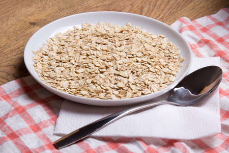 close up of raw oatmeal in plate with spoon on table