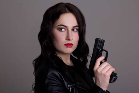 portrait of young beautiful woman with gun over grey background