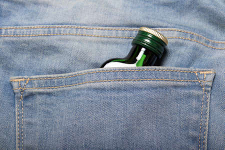alcoholism concept - bottle with alcohol in back pocket of blue jeansの写真素材