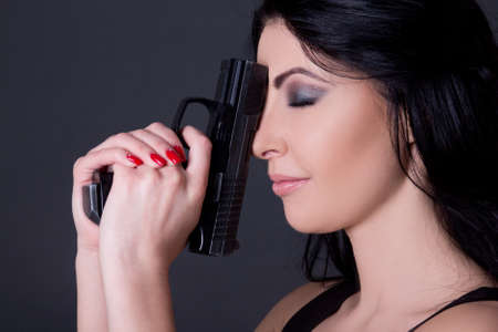 close up portrait of young beautiful woman with gun over grey backgroundの写真素材