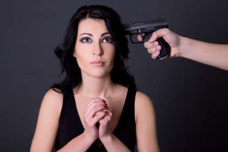 young beautiful woman hostage and male hand with gun over grey backgroundの写真素材