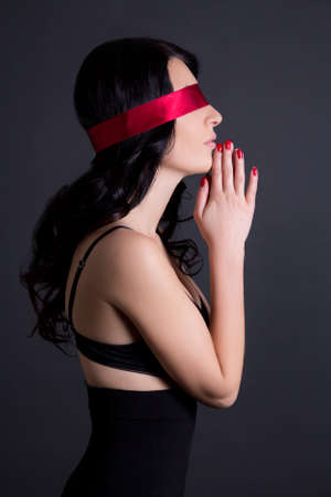 portrait of young beautiful sexy woman in black lingerie with red ribbon on eyes over grey backgroundの写真素材