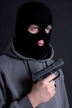man criminal in black mask with gun over grey backgroundの写真素材
