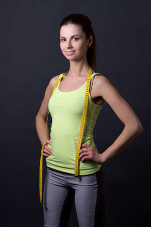 young beautiful slim sporty woman with measure tape over grey backgroundの写真素材
