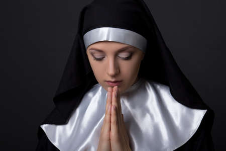 portrait of young beautiful praying nun over grey background