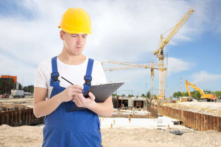 portrait of young handsome man in  builder uniform with clipboard and pencil