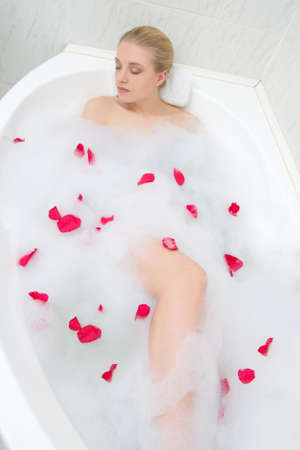 beautiful woman relaxing in bath with red rose flower petals