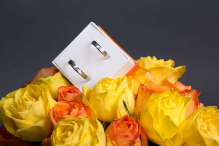 bouquet of rose flowers and wedding rings in box over grey background