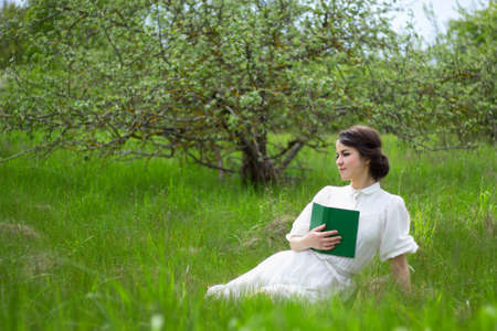 young beautiful woman in white vintage dress with book on summer meadowの写真素材