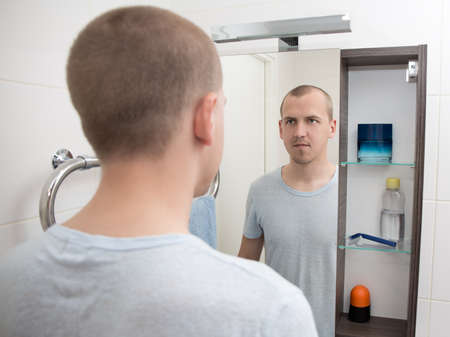 young handsome man looking at mirror in bathroomの写真素材