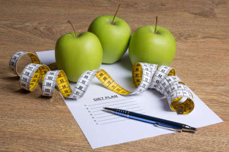 close up of paper with diet plan, green apples and measure tape on wooden tableの写真素材
