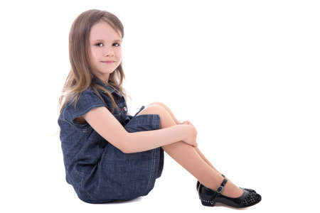 cute little girl in denim dress sitting isolated on white backgroundの写真素材