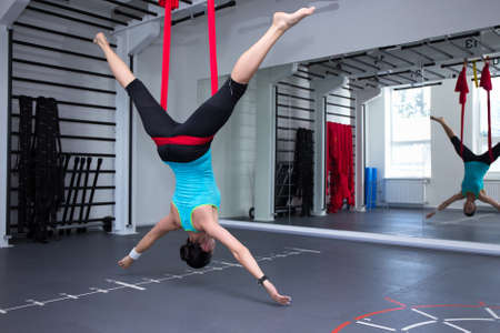 young woman making antigravity yoga exercises in modern gym