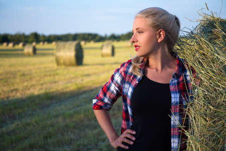 portrait of young beautiful blonde woman in field with haystacksの写真素材