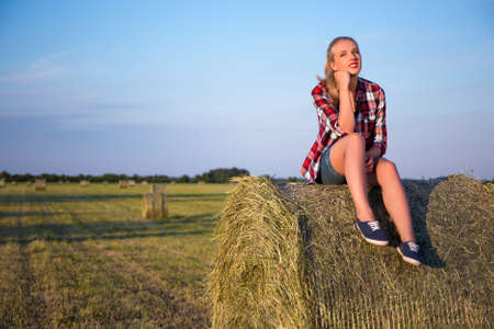 country concept - young beautiful woman sitting on haystack in field