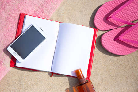 notepad and smart phone with copy space on sandy beach background
