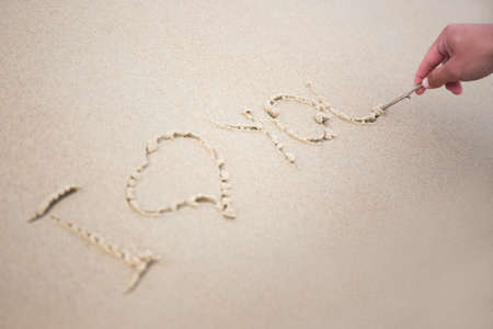 male hand writing words i love you in sand on the beach