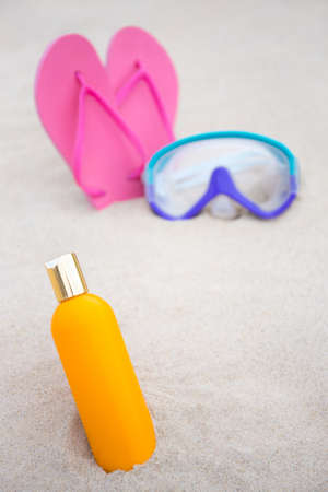 skin care concept - close up of suntan lotion bottle, diving mask and flip flops on summer sandy beachの写真素材